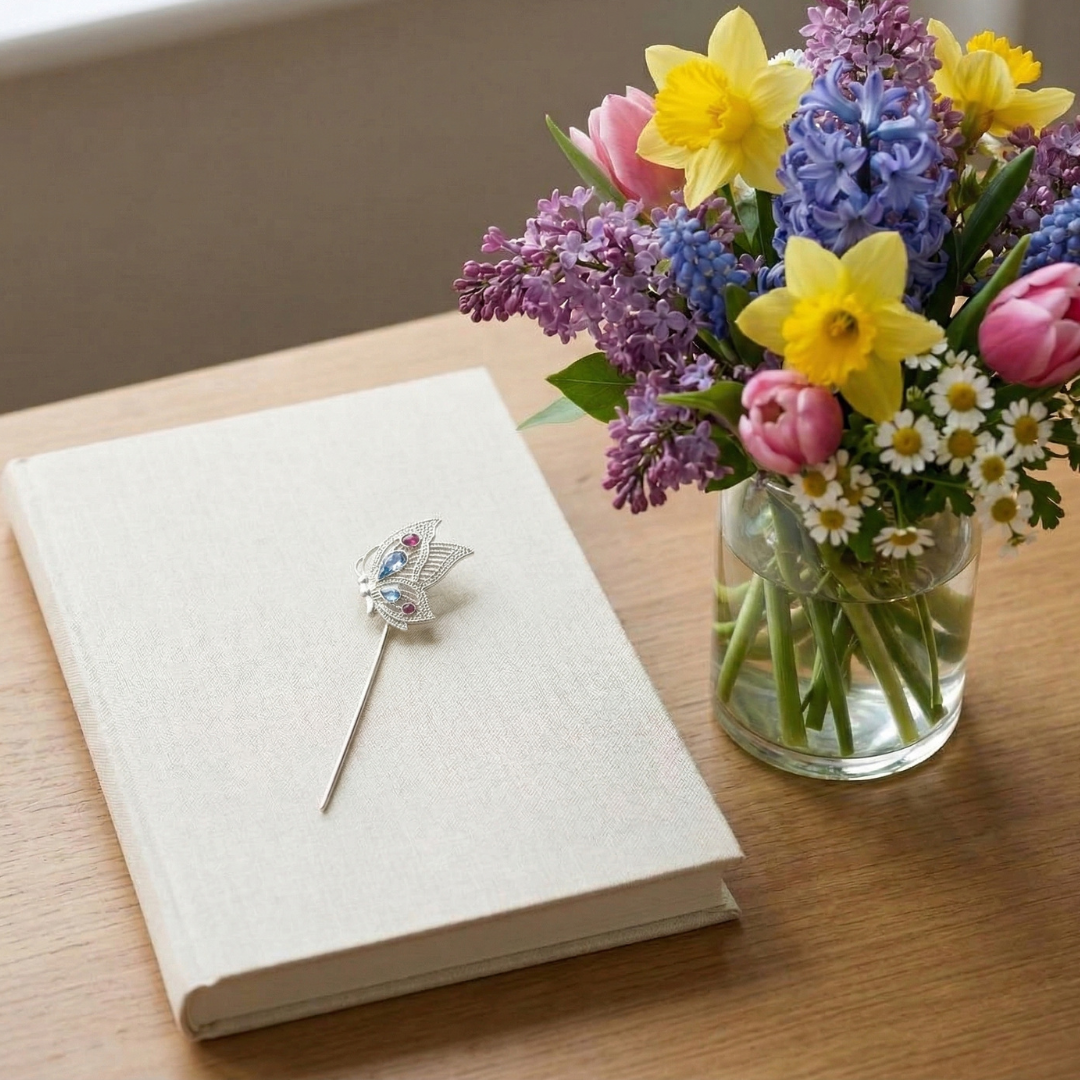 Silver butterfly bookmark with crystals on a book with a vase of flowers on a wooden surface