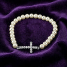 White faux pearl bracelet with a crystal accented cross design on purple fabric