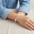 Woman in a denim outfit wearing a white faux pearl bracelet with a crystal accented cross design