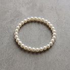 White 8mm Faux Pearl Stretch Bracelet on a textured gray concrete surface.