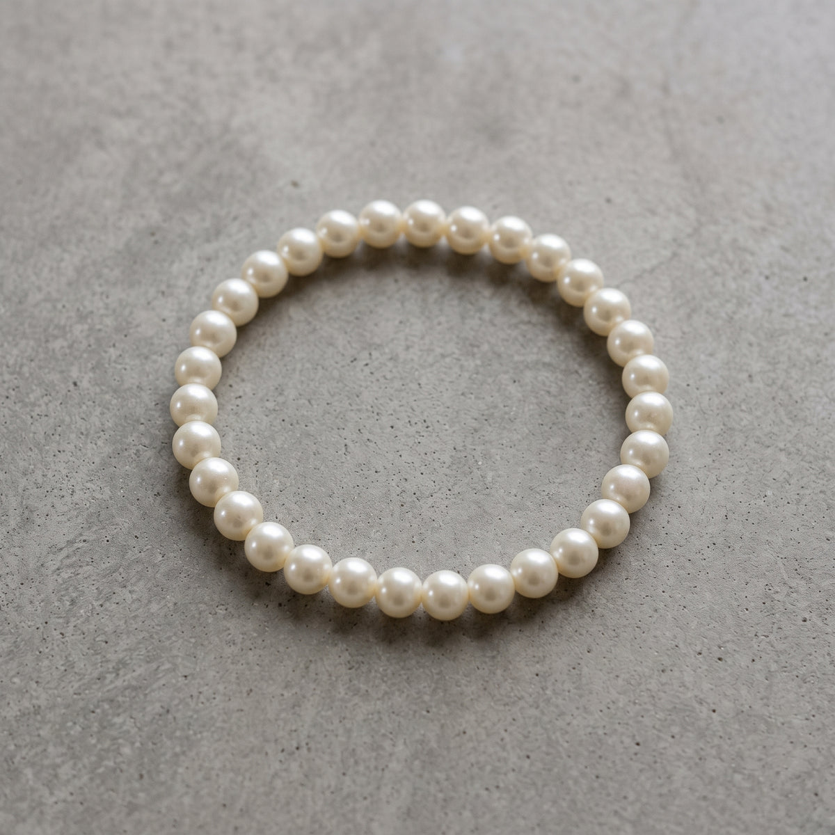 White 8mm Faux Pearl Stretch Bracelet on a textured gray concrete surface.