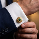 Close-up of a person wearing a gold cufflink with a green gemstone on a white cuff against a dark suit.