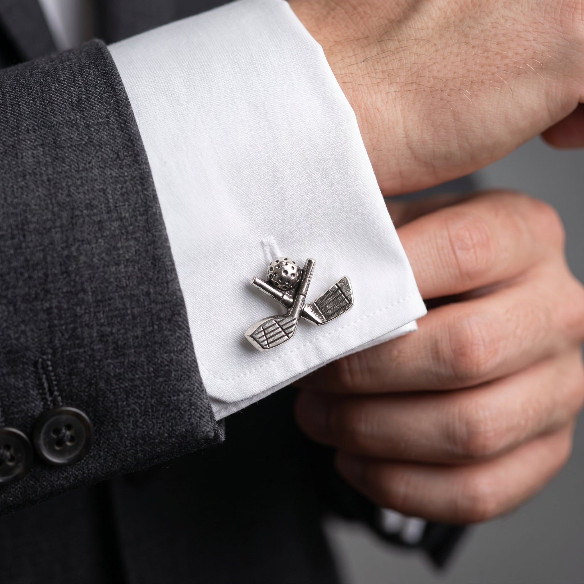 Golf clubs cufflink on a white shirt cuff with a dark suit background