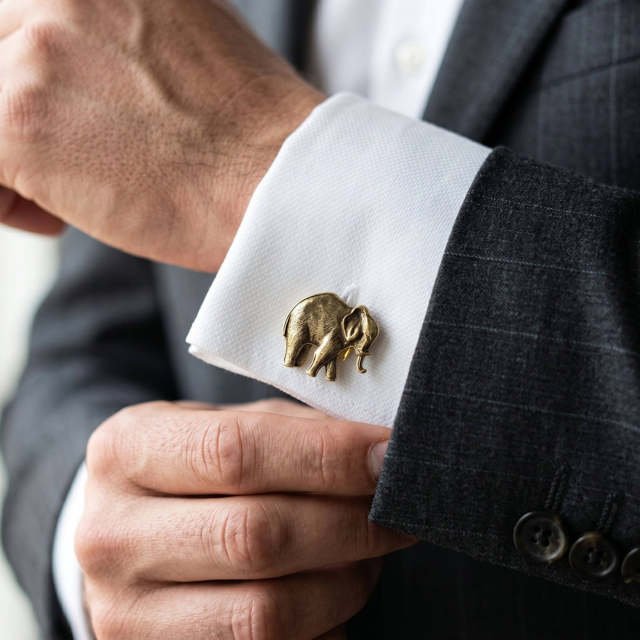 Cufflink with elephant design on a white shirt cuff, worn with a dark suit.