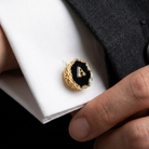 Black enamel cufflink with letter 'A' on a white shirt cuff, held by a hand.