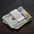 Silver money clip clamps down on US dollar bills on a desk.