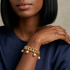 Woman wearing a gold tone pink Faux Pearl Drop Bead Stretch Bracelet on her wrist with a dark blue top