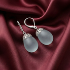 Light blue egg-shaped earrings with silver leverbackings on burgundy satin