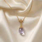 Gold necklace with a translucent egg-shaped pendant against a cream color satin fabric