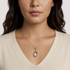 Woman wearing a gold necklace with a translucent egg-shaped pendant against a neutral background
