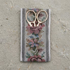 Gold tone scissors in a floral-patterned cloth pouch on a concrete surface