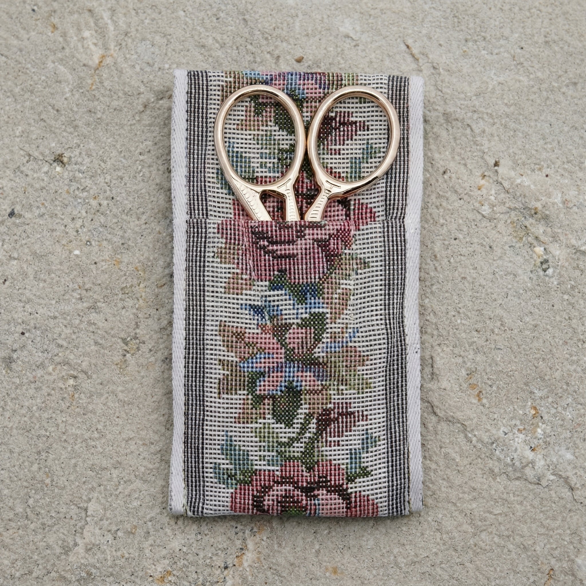 Gold tone scissors in a floral-patterned cloth pouch on a concrete surface