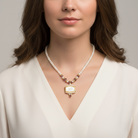 Woman wearing a faux pearl necklace with a flower bouquet pendant against a neutral background