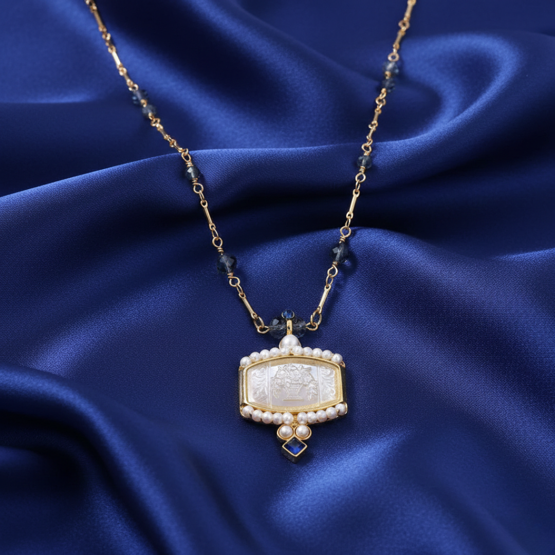 Gold necklace filled with blue beads with a floral bouquet pendant on a blue satin background