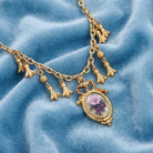 Gold tone Manor House Pink And Purple Rose Pendant Charms Necklace on a blue fabric background