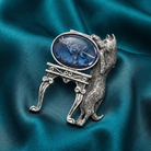 Silver cat and fishbowl brooch with a blue stone on a teal fabric background