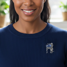 Woman wearing a blue sweater with a decorative brooch featuring a blue stone and silver metal.