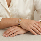 Woman in a white floral top wearing a Manor House Pink & Purple Floral Stone Rose Quartz Gemstone Link Bracelet on her wrist