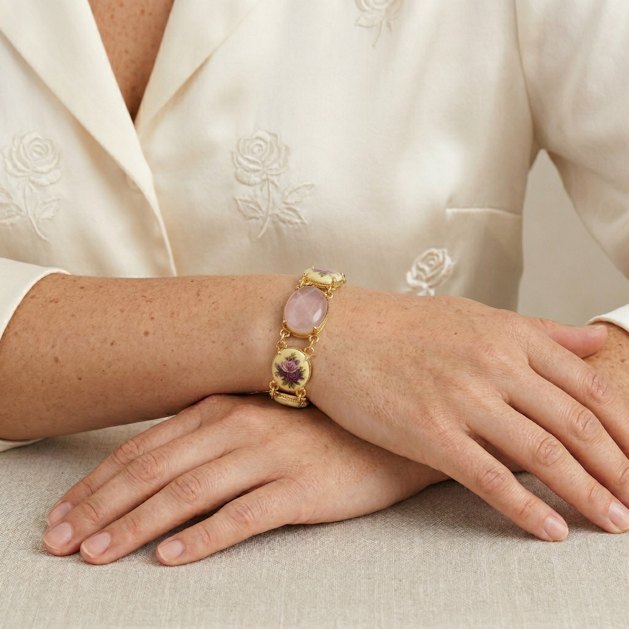Woman in a white floral top wearing a Manor House Pink & Purple Floral Stone Rose Quartz Gemstone Link Bracelet on her wrist
