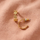 Gold Petite Summer Flower Hoop Earrings, displayed on a textured peach-pink fabric background.