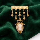 Gold tone brooch with a pink and white cameo on a green fabric background