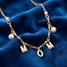 Gold tone necklace with 'MOM' charms and white faux pearl accents on a blue fabric background