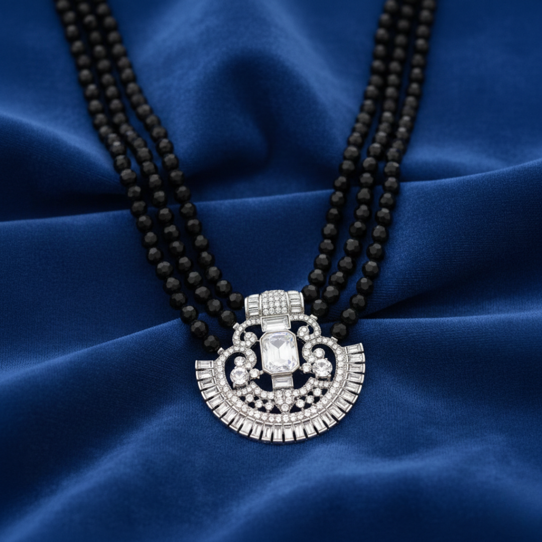 Black beaded necklace with a silver pendant on a blue fabric background