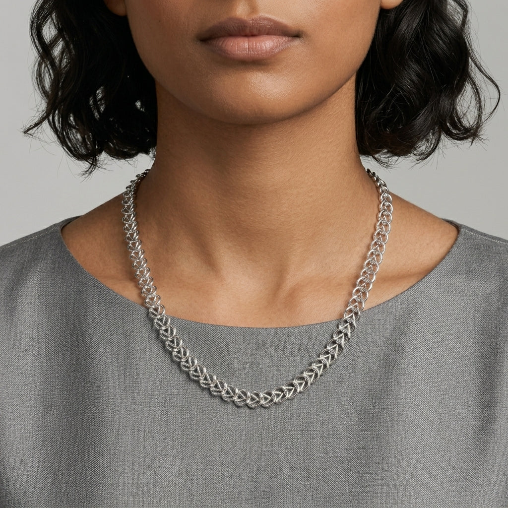 Silver chain necklace worn by a person against a neutral background
