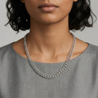 Silver chain necklace worn by a person against a neutral background