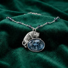 Silver tone Cat And Blue Fish Pendant Necklace with blue bead accents resting on a dark green fabric surface