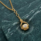 Gold tone 3-Sided Pink Floral Spinner Drop Locket Necklace on a green marble surface
