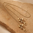 Gold tone Bowling Pins & Ball Face Mask Chain Holder necklace on a textured beige stone surface