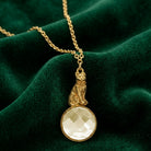 Gold necklace with a topaz crystal and cat pendant on a green velvet background