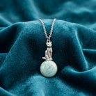 Sitting Cat On Round Turquoise Gemstone Pendant Necklace on a teal fabric background