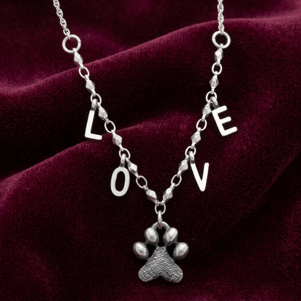 Silver necklace with 'LOVE' pendant and paw charm on a red velvet background