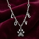 Silver necklace with 'LOVE' pendant and paw charm on a red velvet background