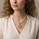 Woman wearing a pearl necklace with a decorative pendant against a neutral background