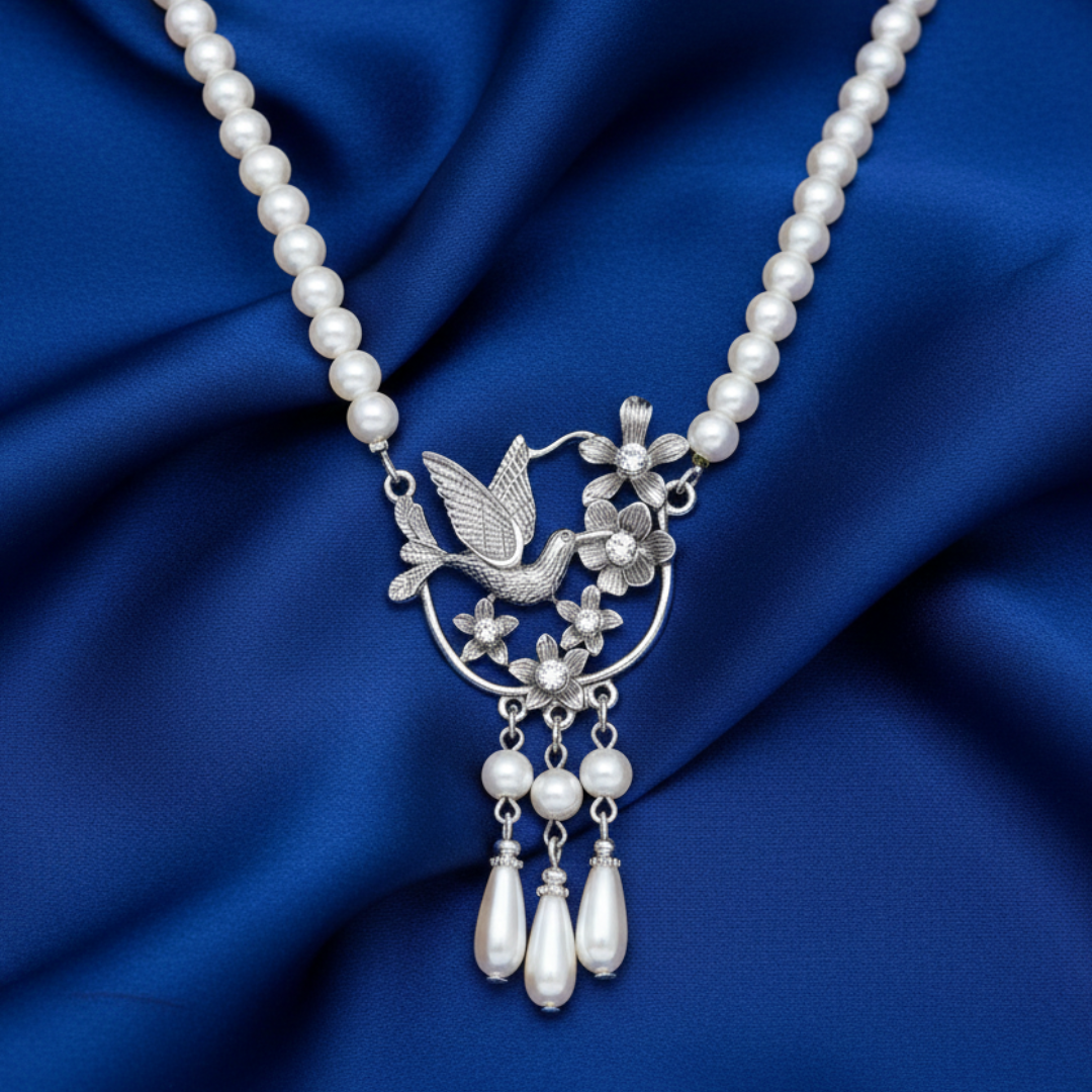 Pearl necklace with a silver hummingbird pendant on a blue fabric background.