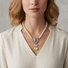Woman wearing a pearl necklace with a silver hummingbird pendant against a neutral background.