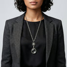 Person wearing a black top and gray blazer with silver tone Filigree Heart And Round Magnifying Glass Pendant Necklace