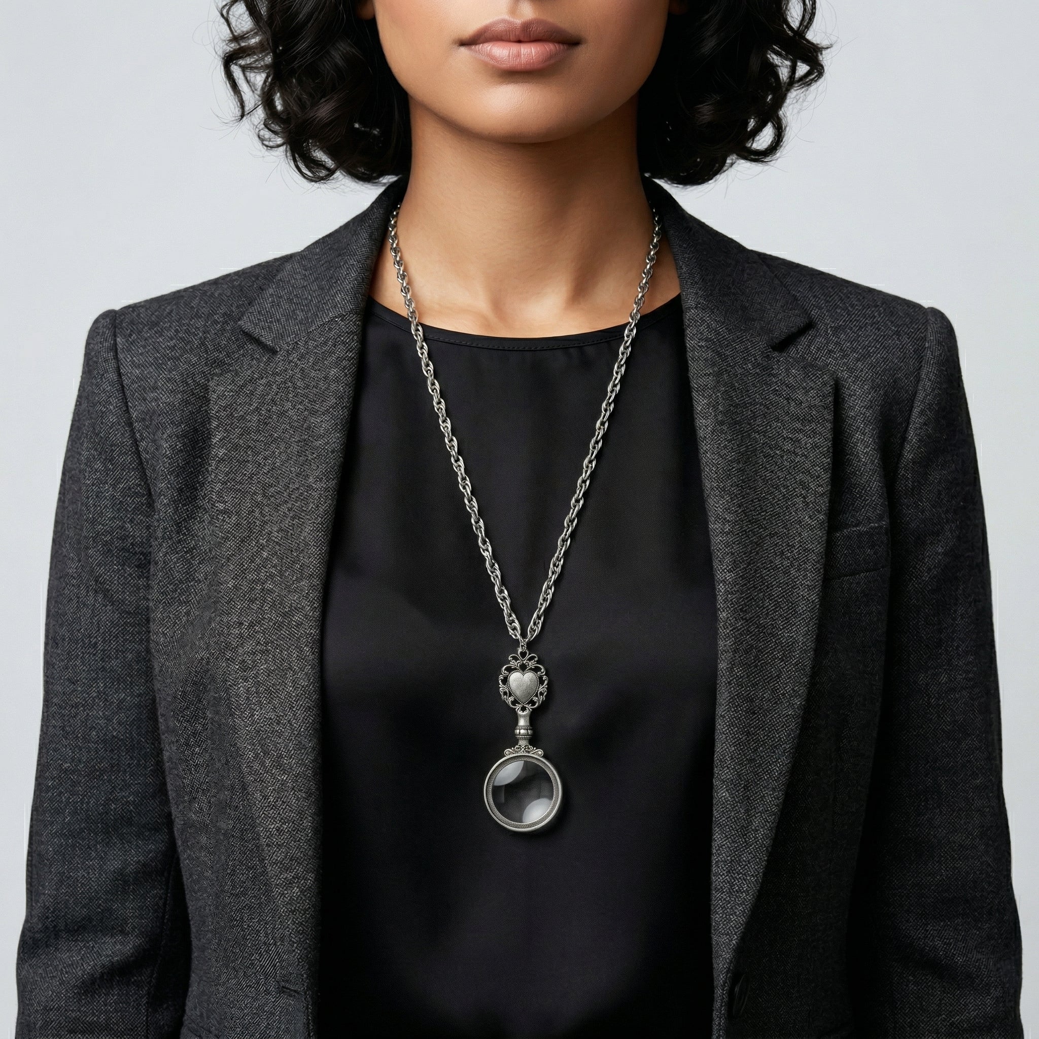 Person wearing a black top and gray blazer with silver tone Filigree Heart And Round Magnifying Glass Pendant Necklace