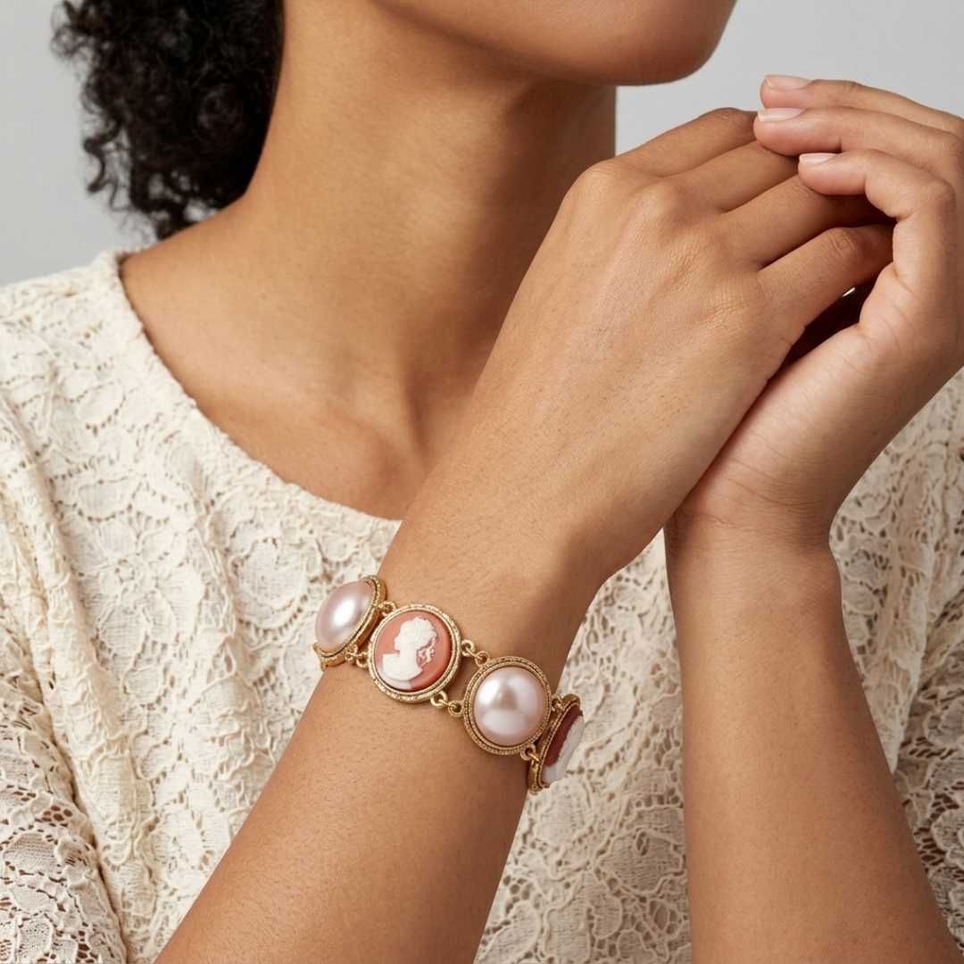 Close-up of a person wearing a gold bracelet with pink pearls and cameo design against a neutral background