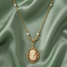 Gold faux pearl necklace with a cameo pendant on a green satin background