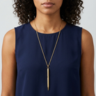 Woman wearing a navy blue sleeveless top with a gold pen pendant necklace against a plain background