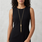 Woman wearing a black sleeveless dress with a long gold necklace that has a red cameo design on a pen pendant against a neutral background