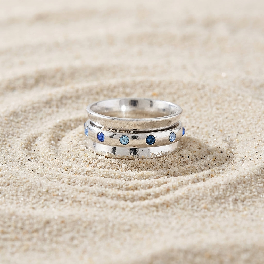 Blue Aqua Marine Crystal Anxiety Spinner Ring resting in raked sand.