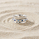 Blue Aqua Marine Crystal Anxiety Spinner Ring resting in raked sand.