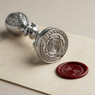 Silver tone rose wax seal stamp with red wax seal on a beige background