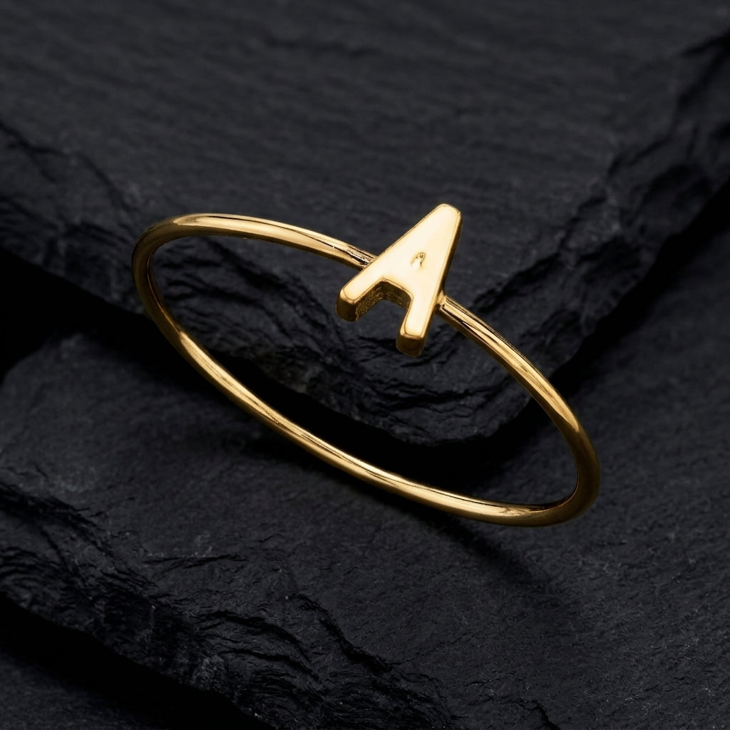 Gold tone initial lettered "A" ring that is resting on a dark stone surface