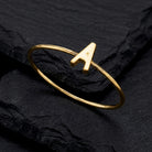 Gold tone initial lettered "A" ring that is resting on a dark stone surface